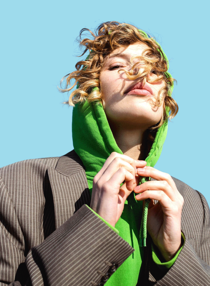 Blond Curly-Haired Girl in Green Hoodie and Elegant Jacket on a Windy Day